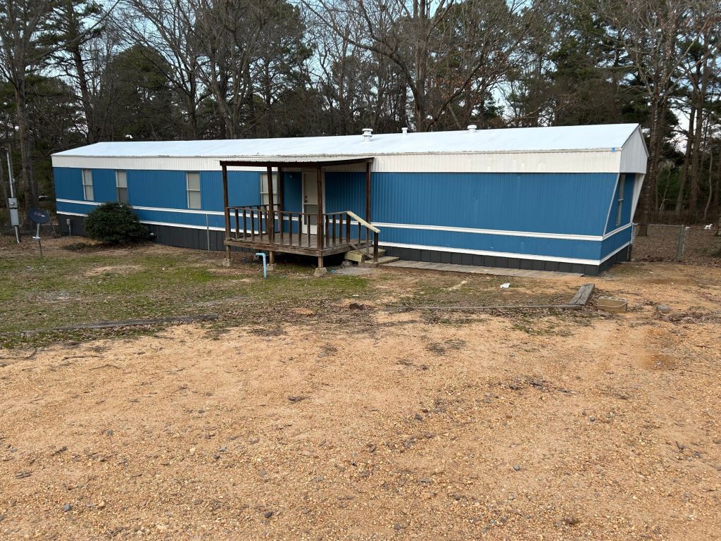 A blue and white mobile home with a porch, situated in a grassy area surrounded by trees.